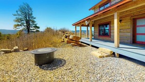 A wooden cabin with a covered porch, a fire pit, and a view of the surrounding landscape. - Ridgetop mountain-view home on 5 acres with Gas Grill, AC & fireplace (Pagosa Springs)