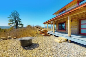 A wooden cabin with a covered porch, a fire pit, and a view of the surrounding landscape. - Ridgetop mountain-view home on 5 acres with Gas Grill, AC & fireplace (Pagosa Springs)