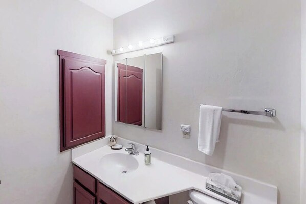 Une salle de bain avec un lavabo blanc, un miroir et un meuble-lavabo doté d’un porte-serviettes.