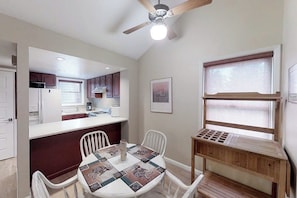 A compact kitchen with a dining area, a ceiling fan, and a window with blinds.