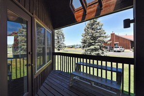 Une terrasse en bois avec un banc, une porte vitrée et une vue sur un parking bordé d’arbres et sur un immeuble.