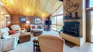 Un salón acogedor con techo de madera, chimenea y ventanas amplias.
