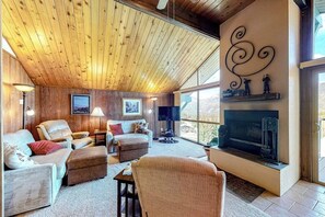 Ein gemütliches Wohnzimmer mit Holzboden, einem Kamin und großen Fenstern.