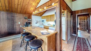 Una cocina con techo de madera, barra con taburetes y microondas.