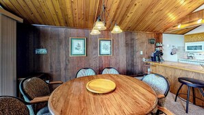 Techo de madera, una mesa redonda de madera con una tabla de cortar y una barra con taburetes.
