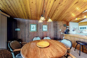 Eine Holzbalkendecke, ein runder Holztisch mit Schneidebrett und eine Bar mit Hockern.