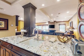 Eine Küche mit Granit Arbeitsplatten, einem Spülbecken, einer hohen Säule und einem Essbereich mit einer Couch und einem Tisch.