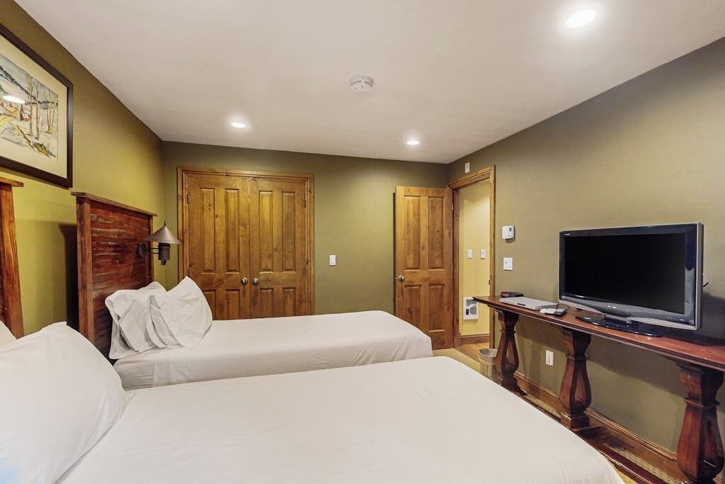 A hotel room with two beds, wooden wardrobes, a television on a wooden stand, and a ceiling light.