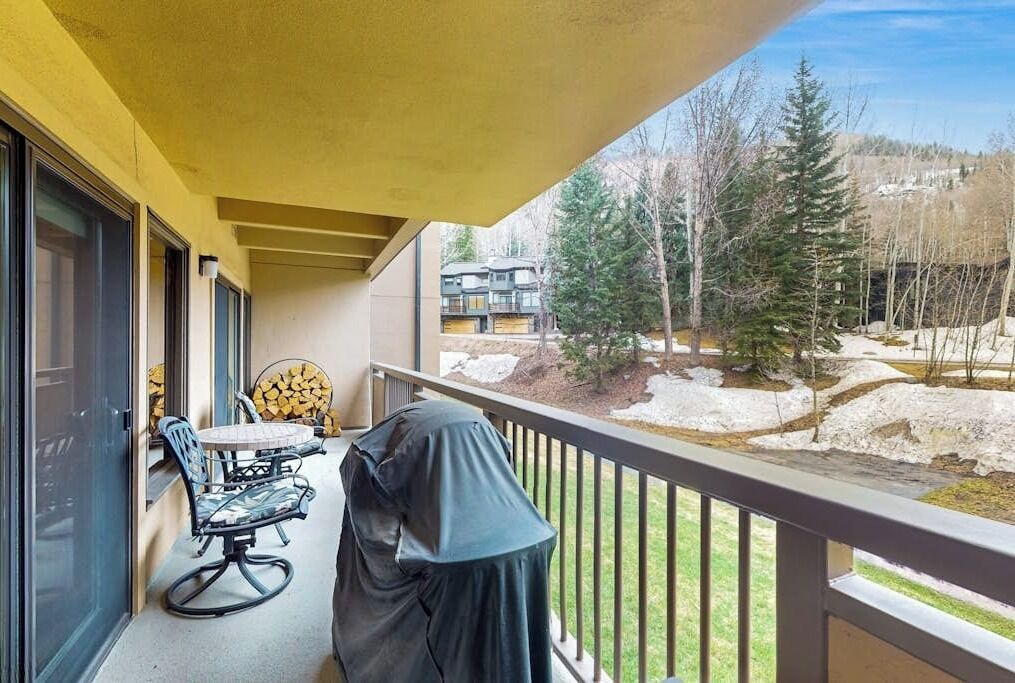 Ein Balkon mit überdachtem Grill, Sitzgelegenheit im Freien und Blick auf eine verschneite Landschaft mit Bäumen und Gebäuden.