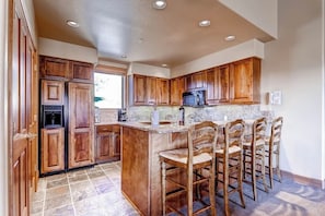 A kitchen with wooden cabinets, a granite countertop, a built-in microwave, and a bar area with stools. - Spacious ski-In/out condo w/free WiFi, shared pool/hot tub/gym (Steamboat Springs)