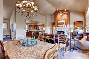 A spacious living room with a large dining table, comfortable seating, a fireplace, and a kitchen in the background. - Spacious ski-In/out condo w/free WiFi, shared pool/hot tub/gym (Steamboat Springs)