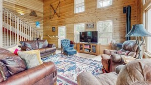 Ein Holzblockhaus-Interieur mit Kamin, Ledersofas, einem Fernseher und einer Treppe.