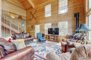 Ein Holzblockhaus-Interieur mit Kamin, Ledersofas, einem Fernseher und einer Treppe.