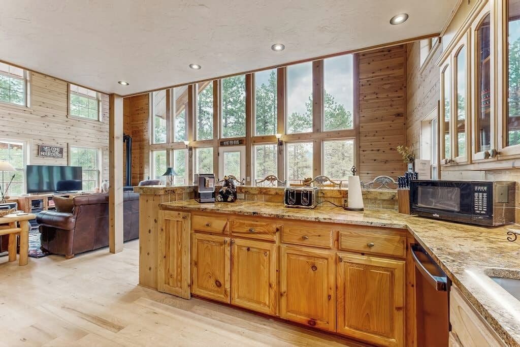 Une cuisine spacieuse dotée de meubles en bois, d’un plan de travail en granit et de grandes fenêtres offrant une vue sur l’extérieur.