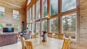 Ein Holzblockhaus-Interieur mit Esstisch, Stühlen, einer Couch und einem Fernseher.