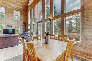 Ein Holzblockhaus-Interieur mit Esstisch, Stühlen, einer Couch und einem Fernseher.