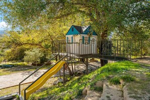 A playground with a slide, a small building with a blue roof, and a fenced area. - Rancho Agave Azul Family Retreat Near Wine Country (Murrieta)