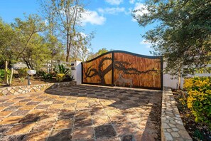 A gated entrance with a wooden fence, stone pathway, and surrounding greenery. - Rancho Agave Azul Family Retreat Near Wine Country (Murrieta)