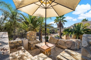 An outdoor seating area with a stone bench, a table, and a large umbrella. - Rancho Agave Azul Family Retreat Near Wine Country (Murrieta)
