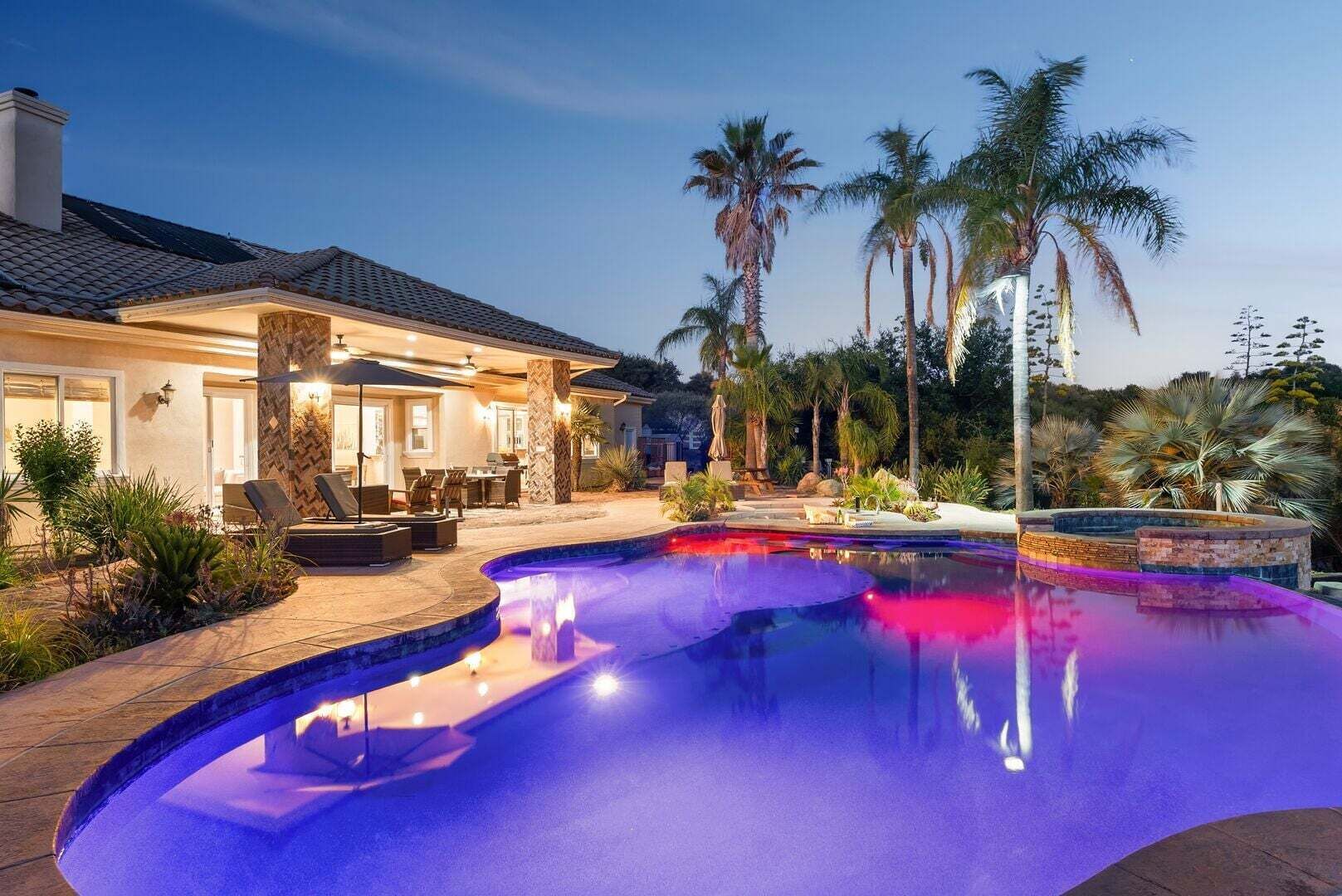 A residential property with a swimming pool, outdoor seating, and palm trees.