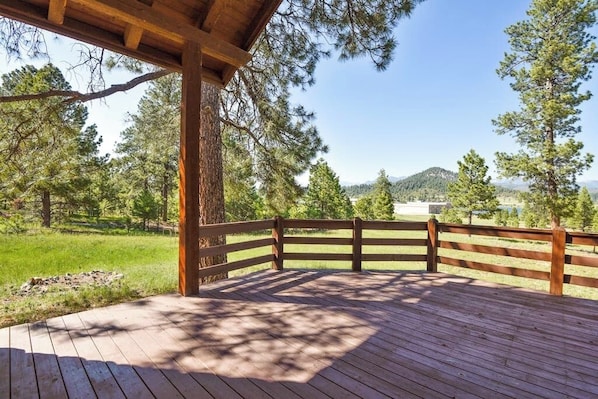 A wooden deck with a wooden railing, surrounded by trees and a clear sky.