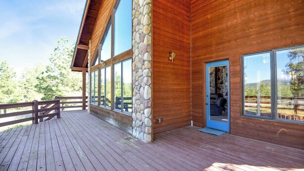 A wooden cabin with large windows, a stone pillar, and a wooden deck. - Dog-friendly cabin with large yard, wood stove, grill & mountain views (Pagosa Springs)