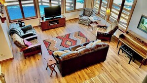 A living room with a large TV, leather sofa, armchairs, a patterned rug, and a wooden coffee table. - Dog-friendly cabin with large yard, wood stove, grill & mountain views (Pagosa Springs)