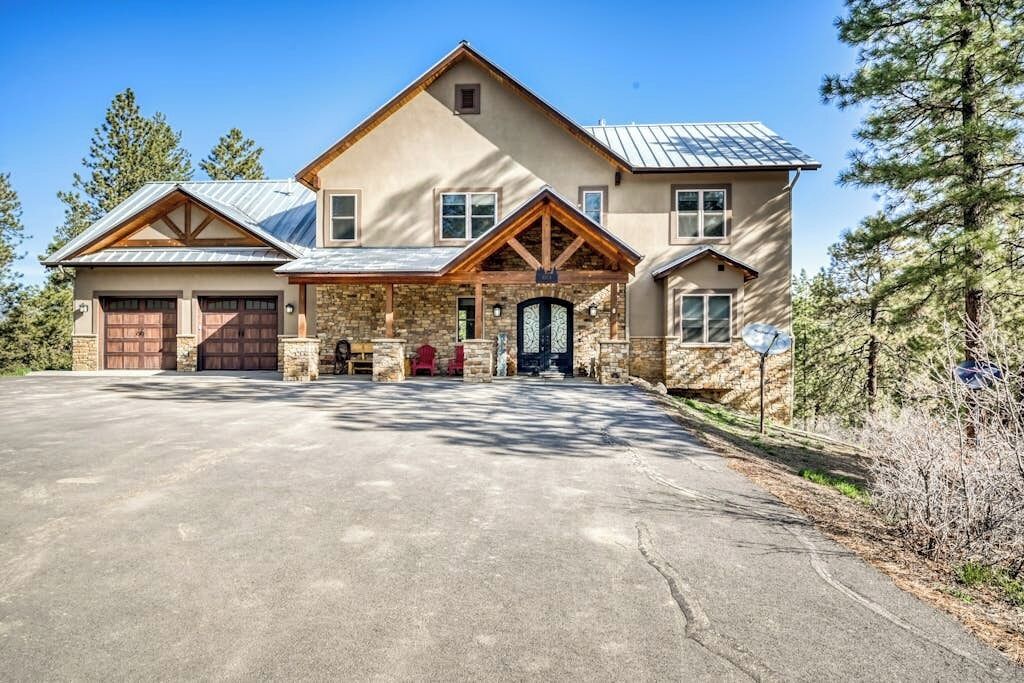 Une grande maison à deux étages, avec une façade en pierre, un porche couvert et un garage.
