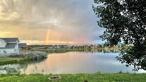 Uitzicht op een meer met stoelen, een tafel, een huis en een regenboog.