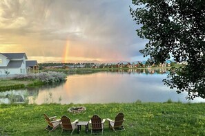 Blick auf einen See mit Stühlen, einem Tisch, einem Haus und einem Regenbogen.
