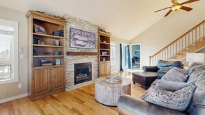Een woonkamer met een open haard, houten planken, een ronde salontafel, een leren bank en een trap.