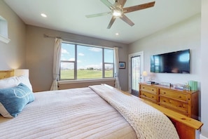 A bedroom with a bed, a ceiling fan, a TV, a window with a view, and a wooden dresser. - Dog-friendly house in central locale on golf course with mountain view & hot tub (Pagosa Springs)