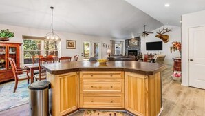 Een ruime keuken met een groot eiland, houten kastjes en een stenen openhaard.