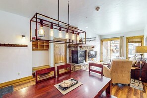 A dining area with a wooden table, chairs, a chandelier, and a fireplace. - Ground-floor, walk-to-lift condo w/ fireplace, W/D & shared pool/hot tubs/gym (Steamboat Springs)