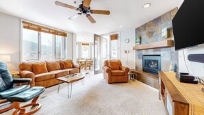 Ein Wohnzimmer mit Sofa, Sessel, Couchtisch, Kamin, Fernseher und Deckenventilator.