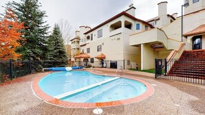 Ein Schwimmbecken mit einer umlaufenden Terrasse, einer Treppe und einem Gebäude mit mehreren Balkonen.