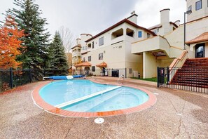Ein Schwimmbecken mit einer umlaufenden Terrasse, einer Treppe und einem Gebäude mit mehreren Balkonen.