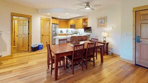 A dining area with a wooden table and chairs, a kitchen in the background, and a ceiling fan. - EagleRidge Lodge 206 Walk-to-gondola condo w/ fireplace, laundry & shared hot tubs/pool/gym/shuttle (Steamboat Springs)