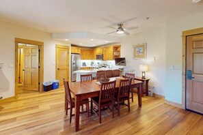 A dining area with a wooden table and chairs, a kitchen in the background, and a ceiling fan. - EagleRidge Lodge 206 Walk-to-gondola condo w/ fireplace, laundry & shared hot tubs/pool/gym/shuttle (Steamboat Springs)
