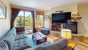 A living room with a sofa, a television, a fireplace, and a balcony with curtains. - EagleRidge Lodge 206 Walk-to-gondola condo w/ fireplace, laundry & shared hot tubs/pool/gym/shuttle (Steamboat Springs)