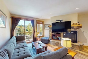 Ein Wohnzimmer mit einer Couch, einem Fernseher, einem Kamin und einem Balkon mit Vorhängen.