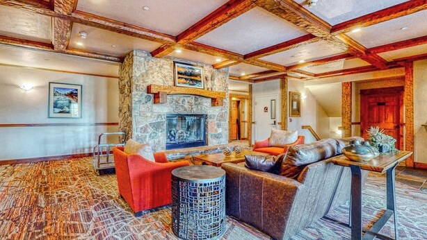 A spacious lobby with a stone fireplace, wooden beams, and a patterned carpet. - EagleRidge Lodge 206 Walk-to-gondola condo w/ fireplace, laundry & shared hot tubs/pool/gym/shuttle (Steamboat Springs)