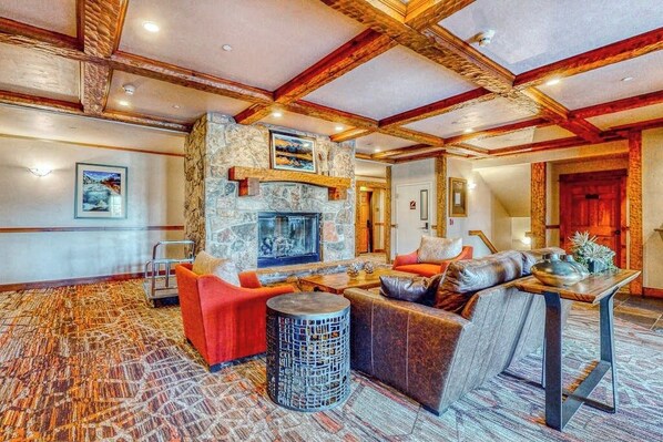 A spacious lobby with a stone fireplace, wooden beams, and a patterned carpet. - EagleRidge Lodge 206 Walk-to-gondola condo w/ fireplace, laundry & shared hot tubs/pool/gym/shuttle (Steamboat Springs)
