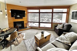 Ein Wohnzimmer mit Kamin, einem an der Wand montierten Fernseher, einer Couch, einem Couchtisch und einem Essbereich mit Stühlen.