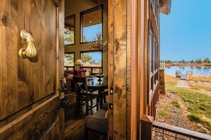 A wooden door with a brass handle, a dining area with a table and chairs, and a view of a lake. - Lakefront home with private dock, mtn & lake views, bikes, fireplace, grill, SUP (Pagosa Springs)