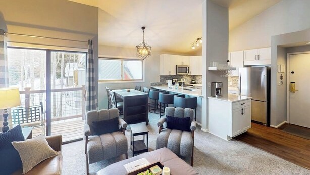 A modern living room with a dining area, kitchen, and large windows. - Conveniently located condo with full kitchen, fast wifi, shared pool & hot tub (Keystone)