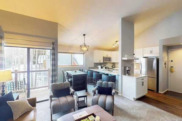 A modern living room with a dining area, kitchen, and large windows. - Conveniently located condo with full kitchen, fast wifi, shared pool & hot tub (Keystone)