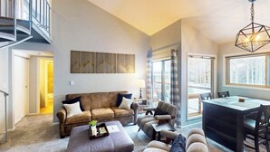 A spacious living area with a sofa, ottoman, and chairs, a dining table, and a staircase. - Conveniently located condo with full kitchen, fast wifi, shared pool & hot tub (Keystone)
