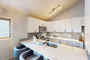 A modern kitchen with white cabinets, a marble countertop, a built-in microwave, and a stainless steel sink. - Conveniently located condo with full kitchen, fast wifi, shared pool & hot tub (Keystone)