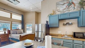 Ein Zimmer mit einem Bett, einem Esstisch mit Schüssel und Servette, einem Kühlschrank, einer Mikrowelle und einem Fenster mit Blick.